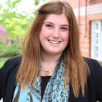 Kailey Kornhauser, a young woman with long red-brown hair wearing a turquoise scarf over a black blouse