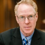 Professor Paul Cassell, a middle-aged white man with red hair wearing a black suit coat and blue collared shirt