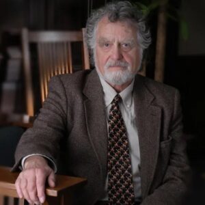 Professor William J. Lockhart, an older man with grey curly hair and a silver beard wearing a brown tweed suit