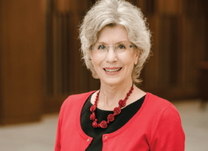 Lori Nelson, an older woman with greying blonde hair wearing a red sweater over a black blouse