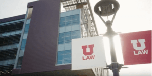 Exterior of Utah Law building with red and white U Law flags hanging from light pole