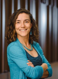 Danya Rumore, a middle-aged woman with dark wavy shoulder-length hair wearing a blue blouse, jacket and necklace