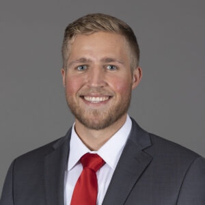 Seth LaPray, a blonde young man wearing a grey jacket with a white shirt and red tie