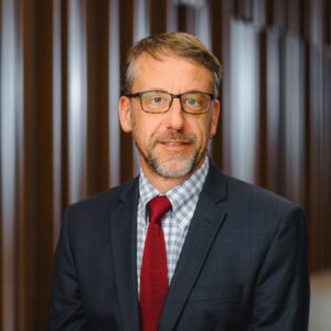 Professor John Ruple, a middle-aged white man with dark blonde hair, and short grey beard with dark spectacles