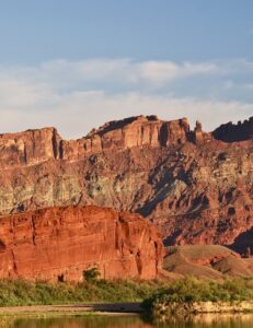 A scenic view of the Colorado River, tall red rock with green desert vegetation and the river at its base