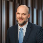 Professor Lincoln Davies, a young bald white man wearing a navy suit and blue tie