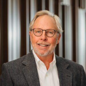 Tom Mitchell, an older white man with short silver hair and a silver beard wearing glasses