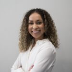 Hannah Bruce, a young black woman with curly brown hair with blond highlights, wears a white collared blouse