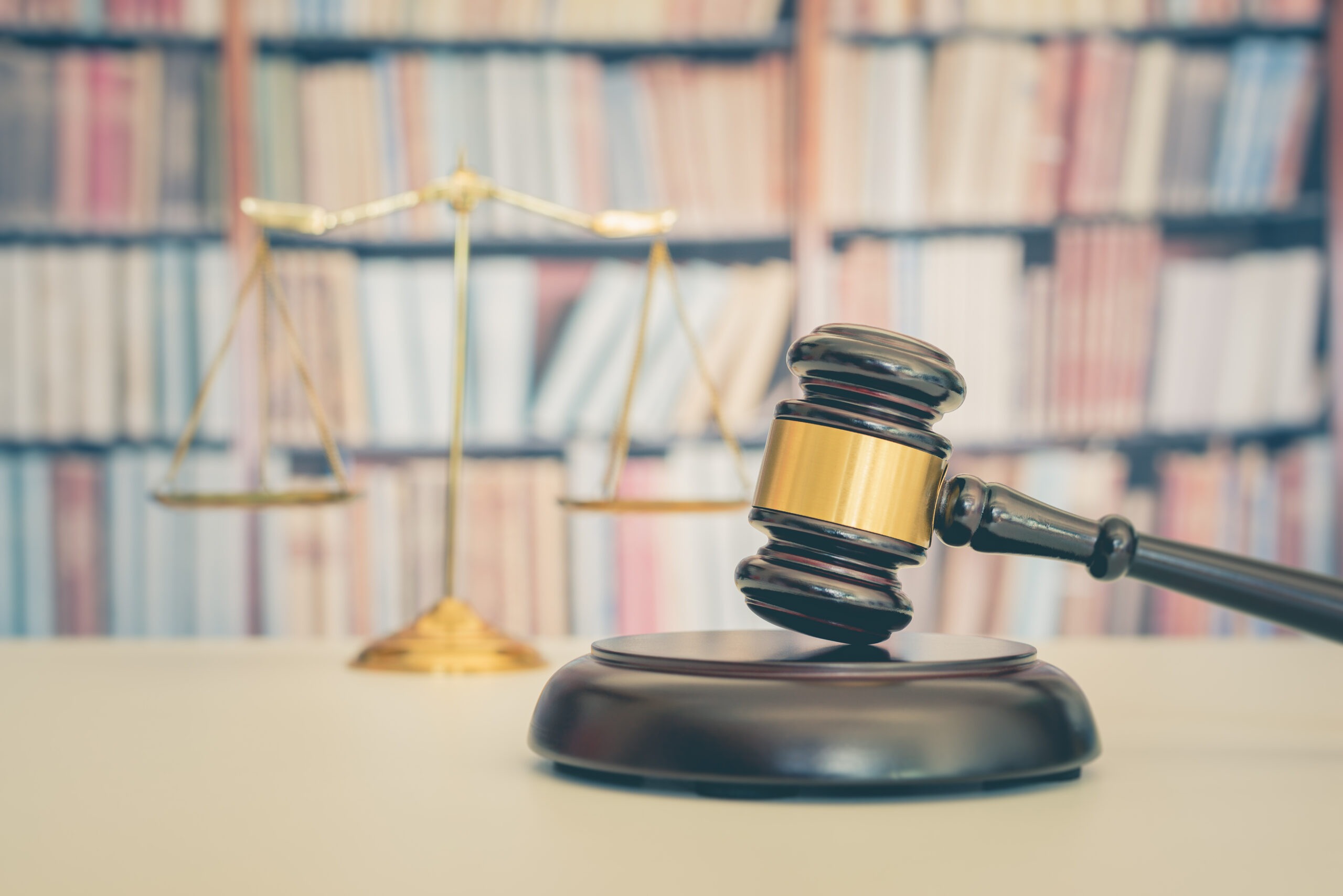 Legal office of lawyers, justice and law concept : Judge gavel or a hammer and a base used by a judge person on a desk in a courtroom with blurred weight scale of justice, bookshelf background behind