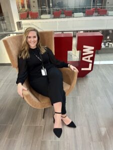 Lexie Kite, a young white woman with shoulder-length wavy blonde hair, sits in a chair near a red block "U" in the law building 