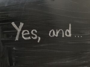 Blackboard with text that says "Yes, and..." written in chalk
