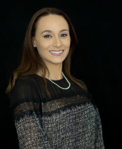 Leah Bench, a young woman with straight dark-brown hair and olive  skin wearing a black and grey blouse