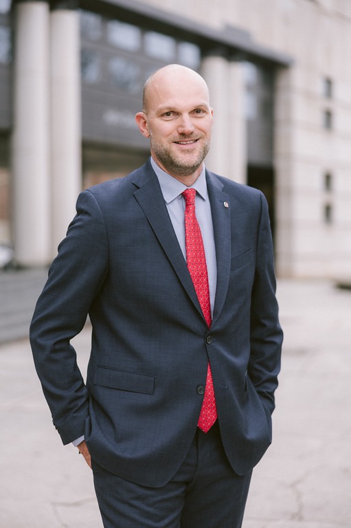 Professor Lincoln Davies, a young bald white man wearing a navy suit and red tie