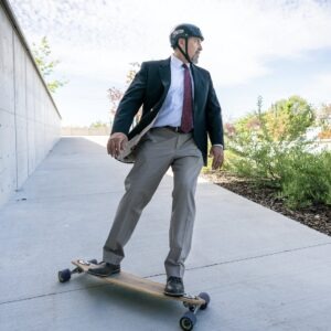 Dean Reyes Aguilar, a middle-aged Hispanic man wearing khaki slacks, a navy blazer and a black helmet white skateboarding down the sidewalk of the Utah Law campus