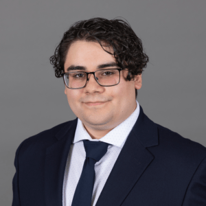 Enrique Martinez, a young Hispanic man with short curly brown hair, brown eyes and black-rimmed glasses