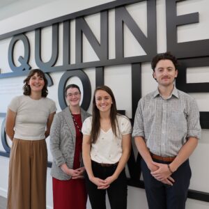 Avery Emery (left), a tall young nonbinary person with short brown hair, Rachel Prickett Passey, a young white woman with dark-brown hair wearing a red dress and grey blazer; Becca Huber, a young white woman with long, straight brown hair wearing a white blouse, and Adam Snow, a young white man with short, dark-brown hair