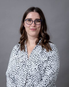 Leigh Ann Bauman, a young white woman with wavy shoulder-length hair and glasses wearing a black and white dotted blouse