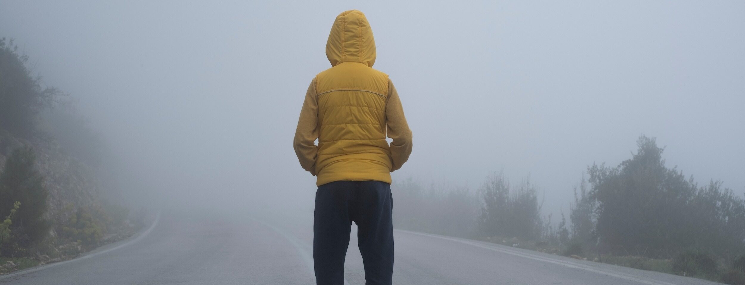 A facing back hoody boy hands in pocket, standing in an abondoned road in air pollution, foggy weather