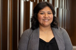 McKell OldBull, a young Native woman with dark-brown shoulder-length hair, brown eyes, and light-brown skin wearing a black blouse and grey blazer