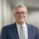 Erik Christiansen, a middle-aged white man with short silver hair and glasses wearing a navy blue suit