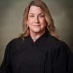 Judge Janet Elledge, a middle-aged woman with shoulder-length curled dark-blonde hair wearing a black judge's robe