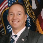 Paul Amann, a middle-aged white man with short dark-brown hair wearing a grey pinstriped suit