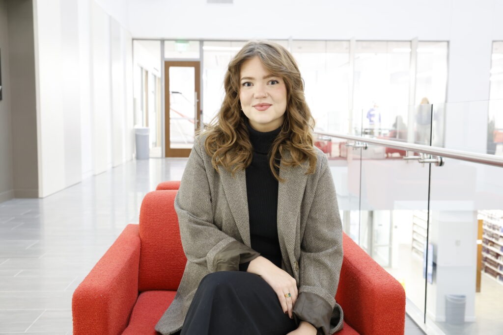 Grace Greene, a young white man with long curled brown hair wearing a herringbone blazer and sitting in a red armchair in the law building